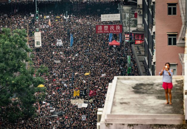 HONG KONG, HONG KONG - 16 Haziran: Hong Kong Çin'de 16 Haziran 2019'da protestocular aşağıdaki caddede yürüyüş yaparken bir kadın çatı katından fotoğraf çekiyor. Pazar günü Hong Kong İcra Kurulu Başkanı Carrie Lam'ın tartışmalı iade yasasının süresiz olarak askıya alınacağını duyurmasına rağmen çok sayıda protestocu yürüyüş yaptı.